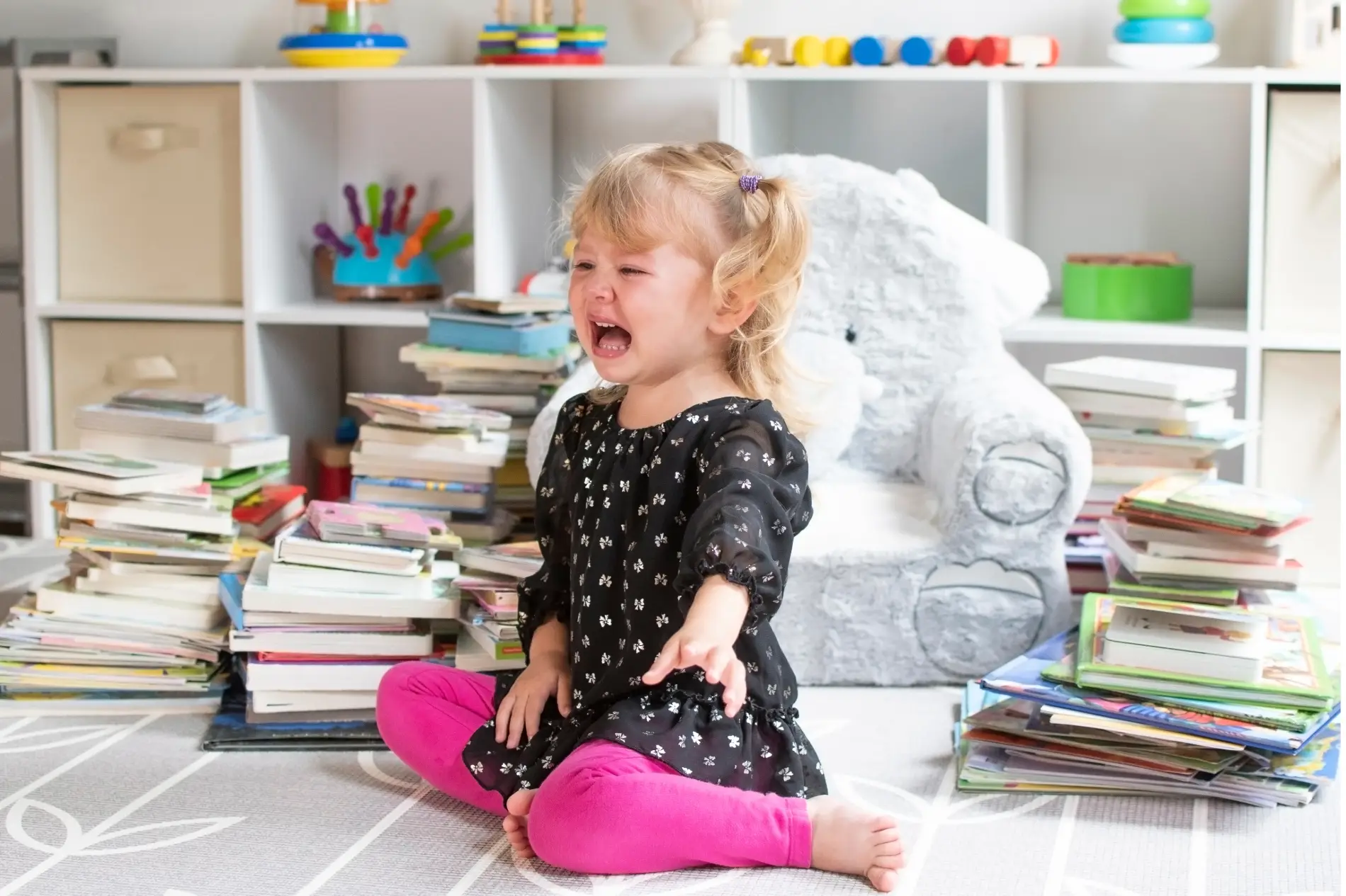 Child sitting on the floor in a room with toys having a tantrum