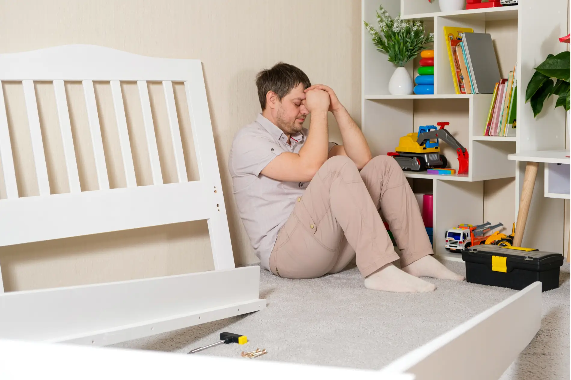 Adult sitting on the floor beside a crib and tools looking overwhelmed