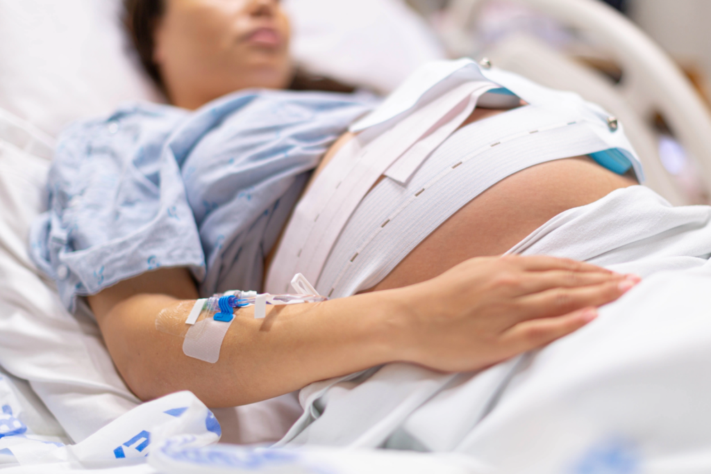 Hospital Birth | I Can THRIVE Counseling Pregnant person resting in a hospital bed with an IV line in the arm and monitoring bands around the abdomen